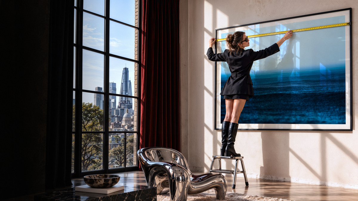 Woman measuring large blue framed wall art in a sunlit contemporary apartment.