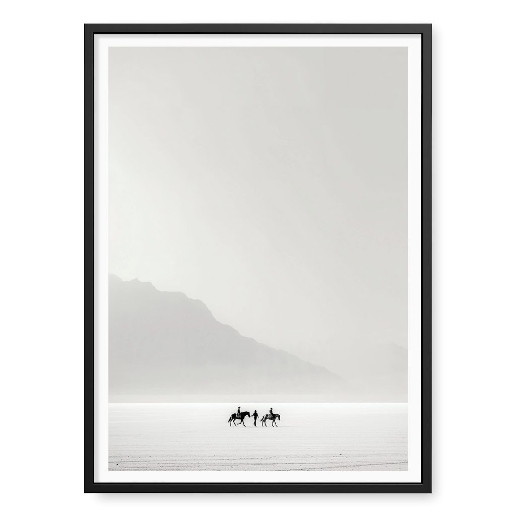 Tiny silhouettes of riders on horseback journeying across a vast white desert landscape, art print titled Destination Unknown in black frame