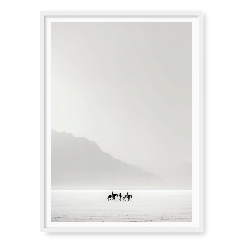 Tiny silhouettes of riders on horseback journeying across a vast white desert landscape, art print titled Destination Unknown in white frame