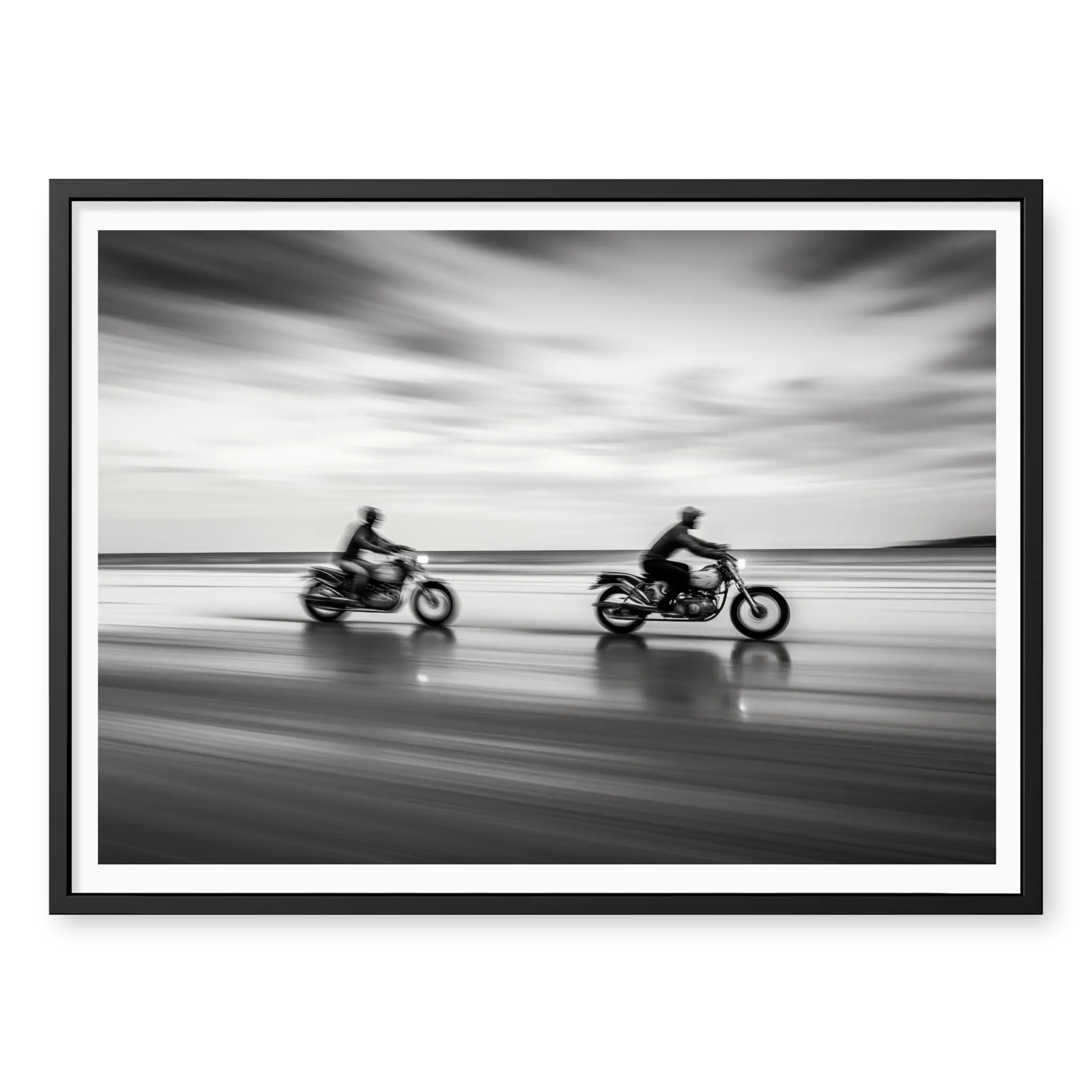 Panning shot of two riders on motorcycles racing along a wet beach with motion blur effect, black and white art print titled Partners in black frame