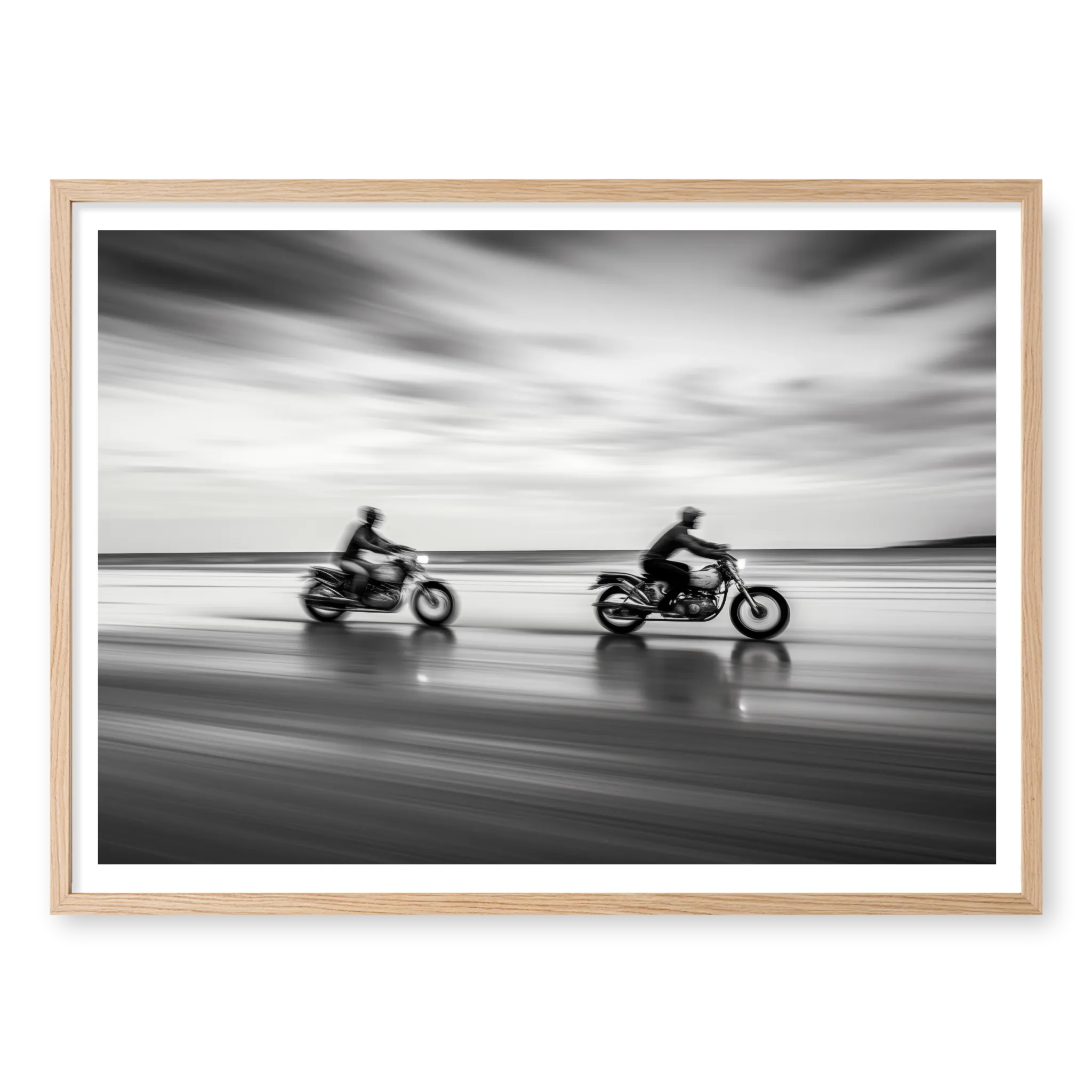 Panning shot of two riders on motorcycles racing along a wet beach with motion blur effect, black and white art print titled Partners in natural oak frame