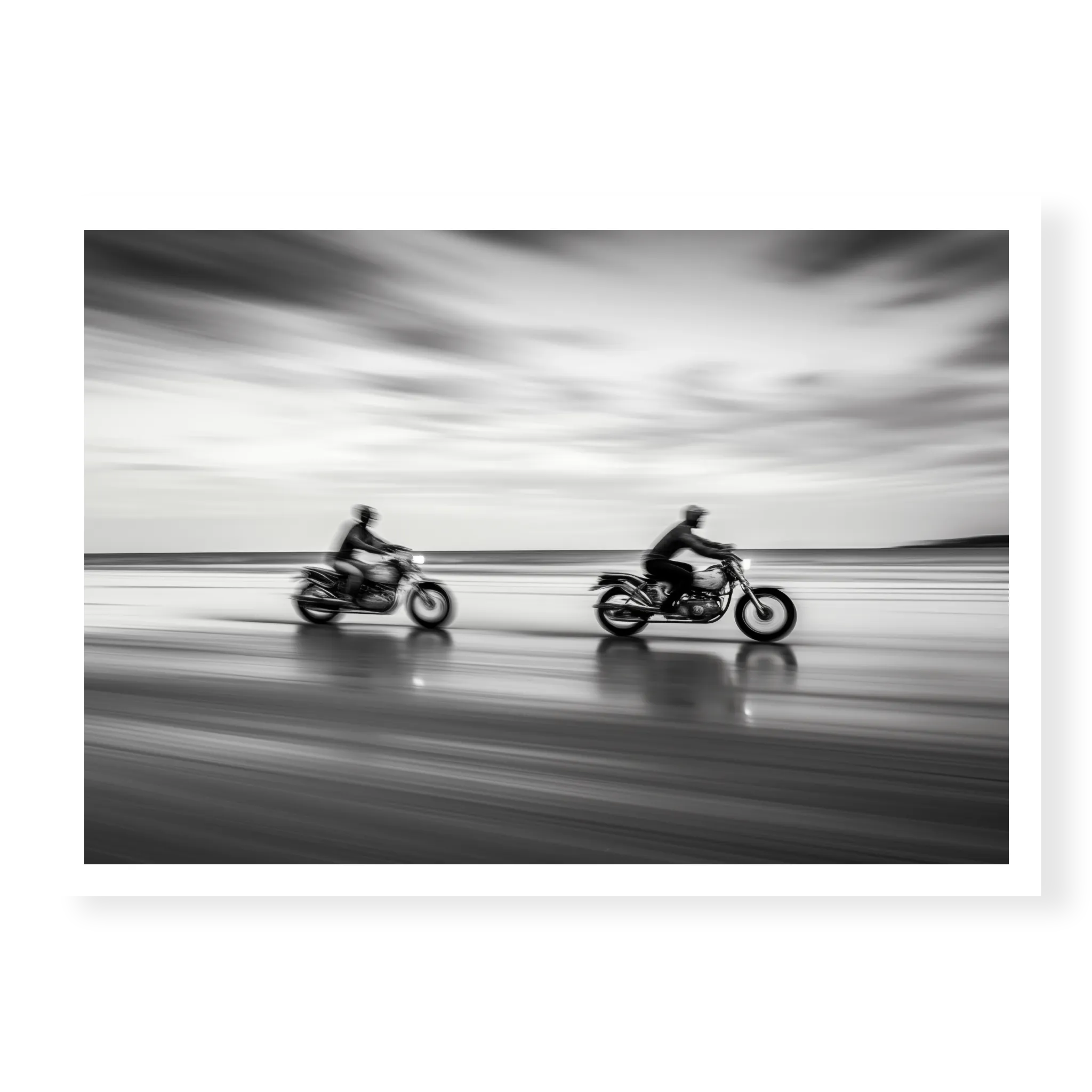 Panning shot of two riders on motorcycles racing along a wet beach with motion blur effect, black and white art print titled Partners