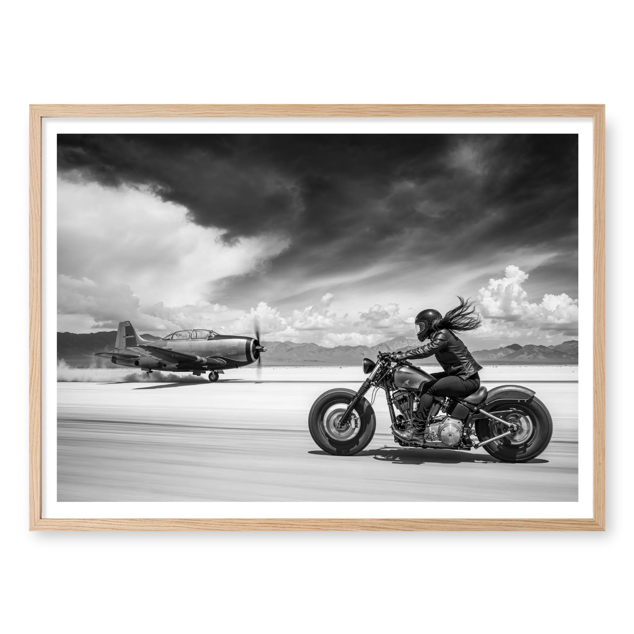 Side view of a rider on a motorcycle racing down a runway alongside a vintage propeller plane, black and white art print titled Ride or Die in natural oak frame