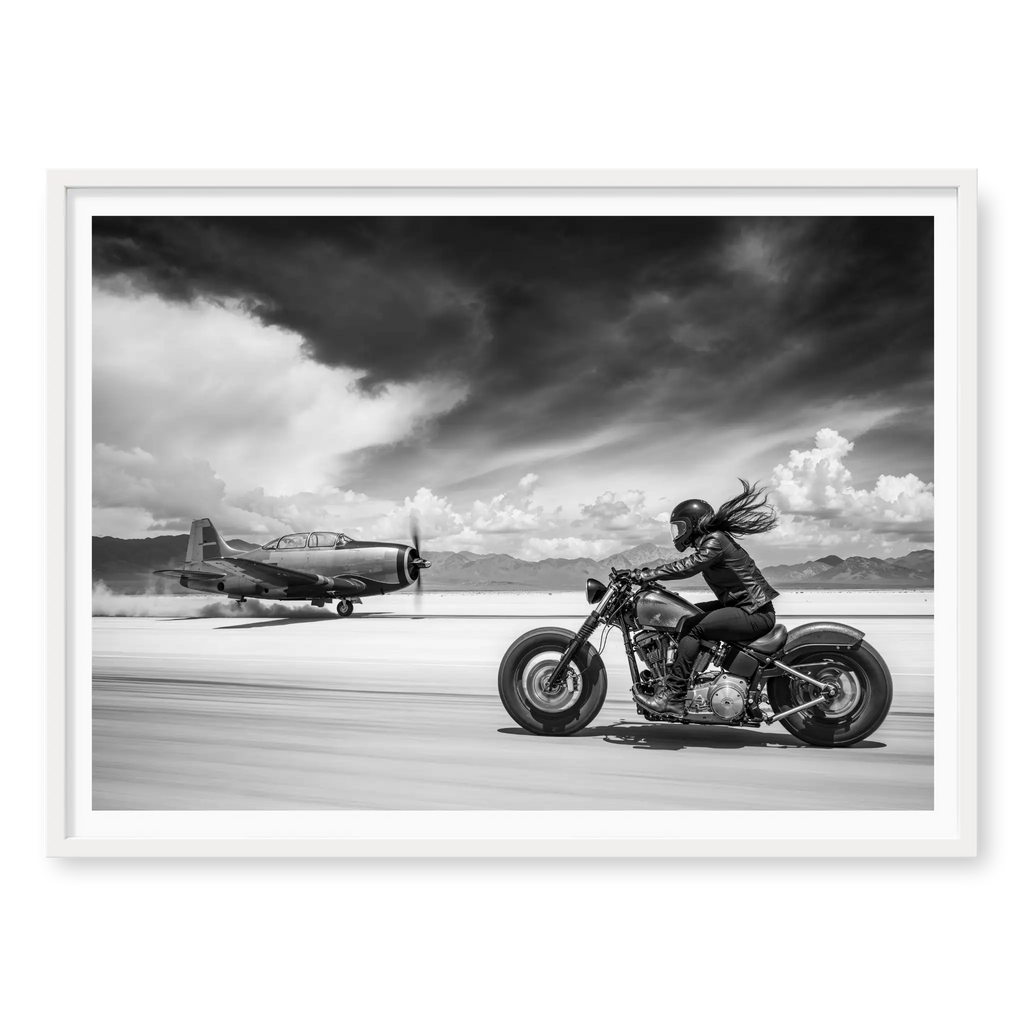 Side view of a rider on a motorcycle racing down a runway alongside a vintage propeller plane, black and white art print titled Ride or Die in white frame