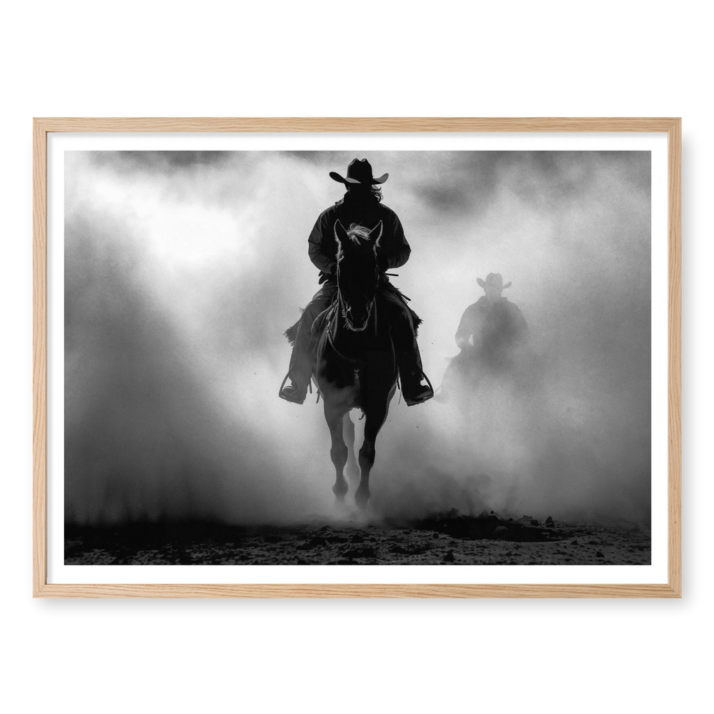 Silhouette of a cowboy riding a horse head-on through thick dust and fog, with a second rider fading into the background, black and white art print titled Searchers in natural oak frame